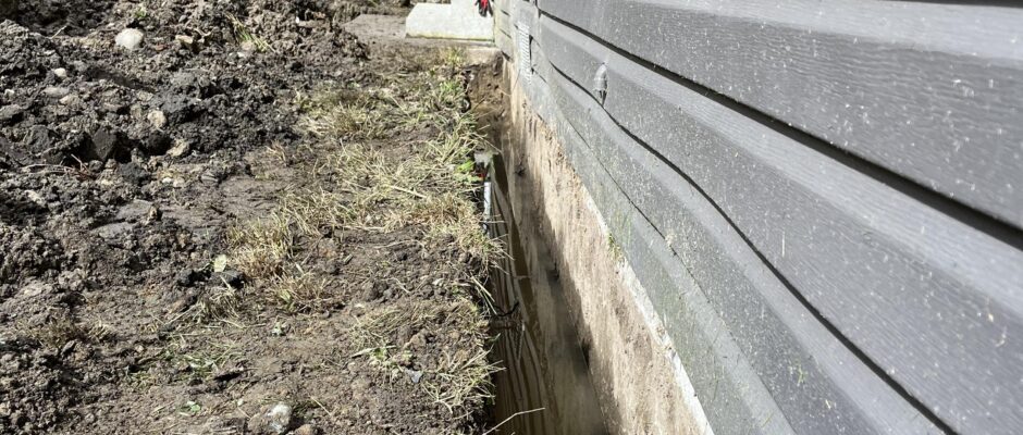 French drain pipe below foundation footing as part of a waterproofing system