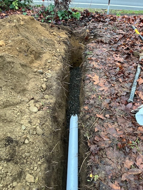 a trench with white perforated pipe before wrapping around in a cloth for Yard drainage solutions in everett, wa